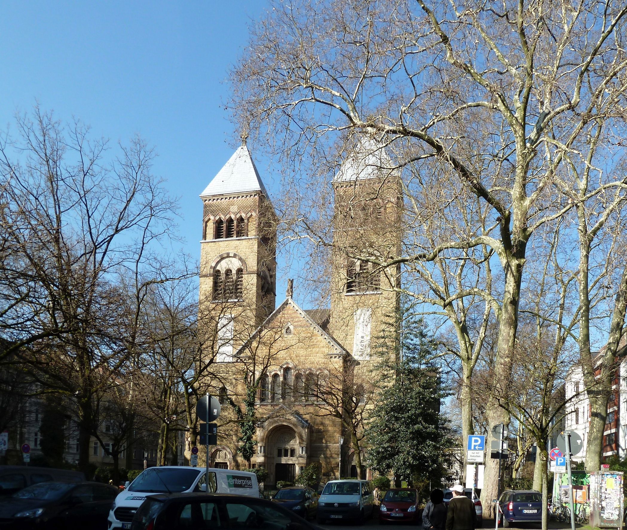 Die Kirche St. Michael mit zwei Türmen am Brüsseler Platz im Belgischen Viertel, davor kahle Platanen.