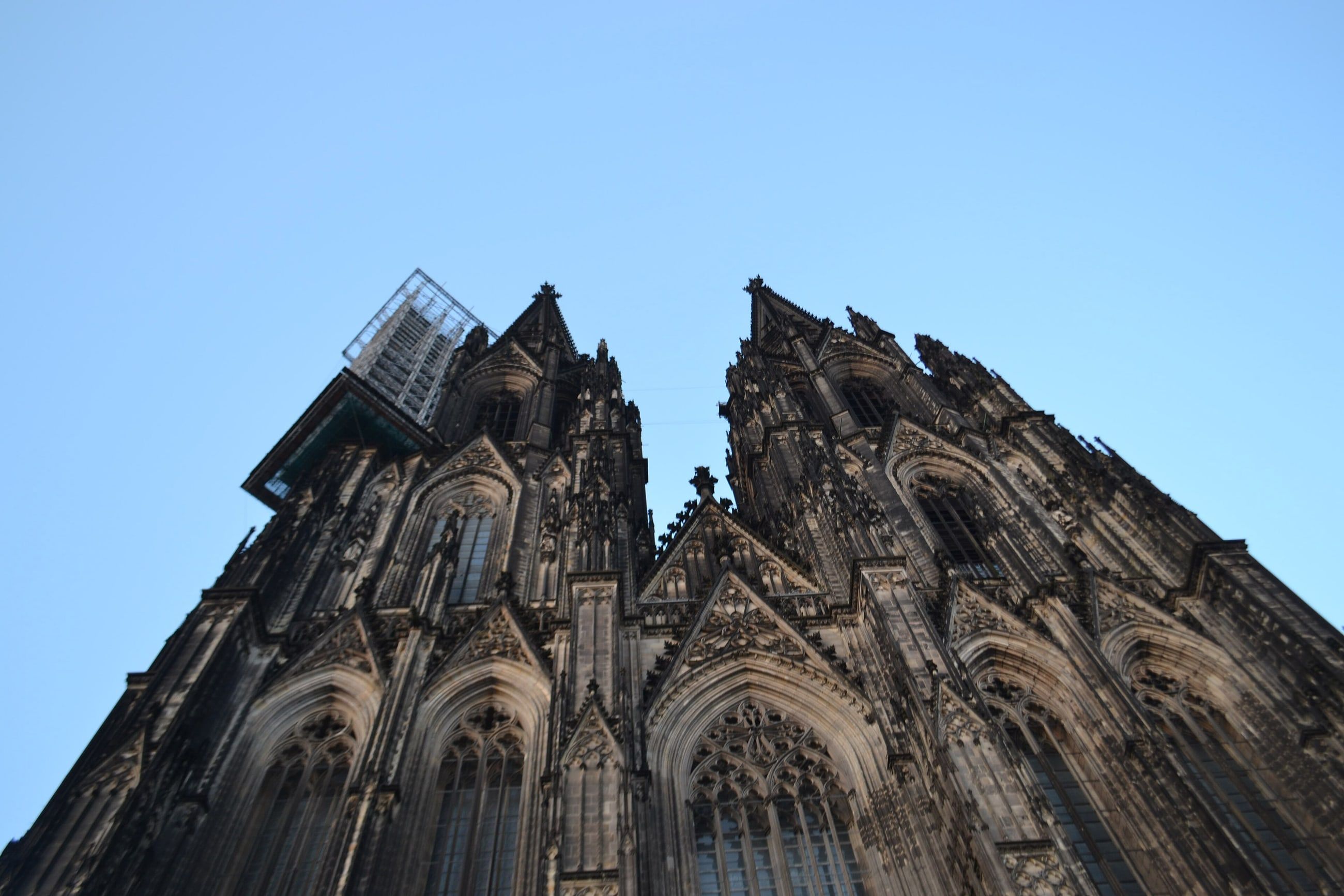 Zwei Türme des Kölner Doms ragen in Froschperspektive neben dem Hauptportal vor blauem Himmel auf.
