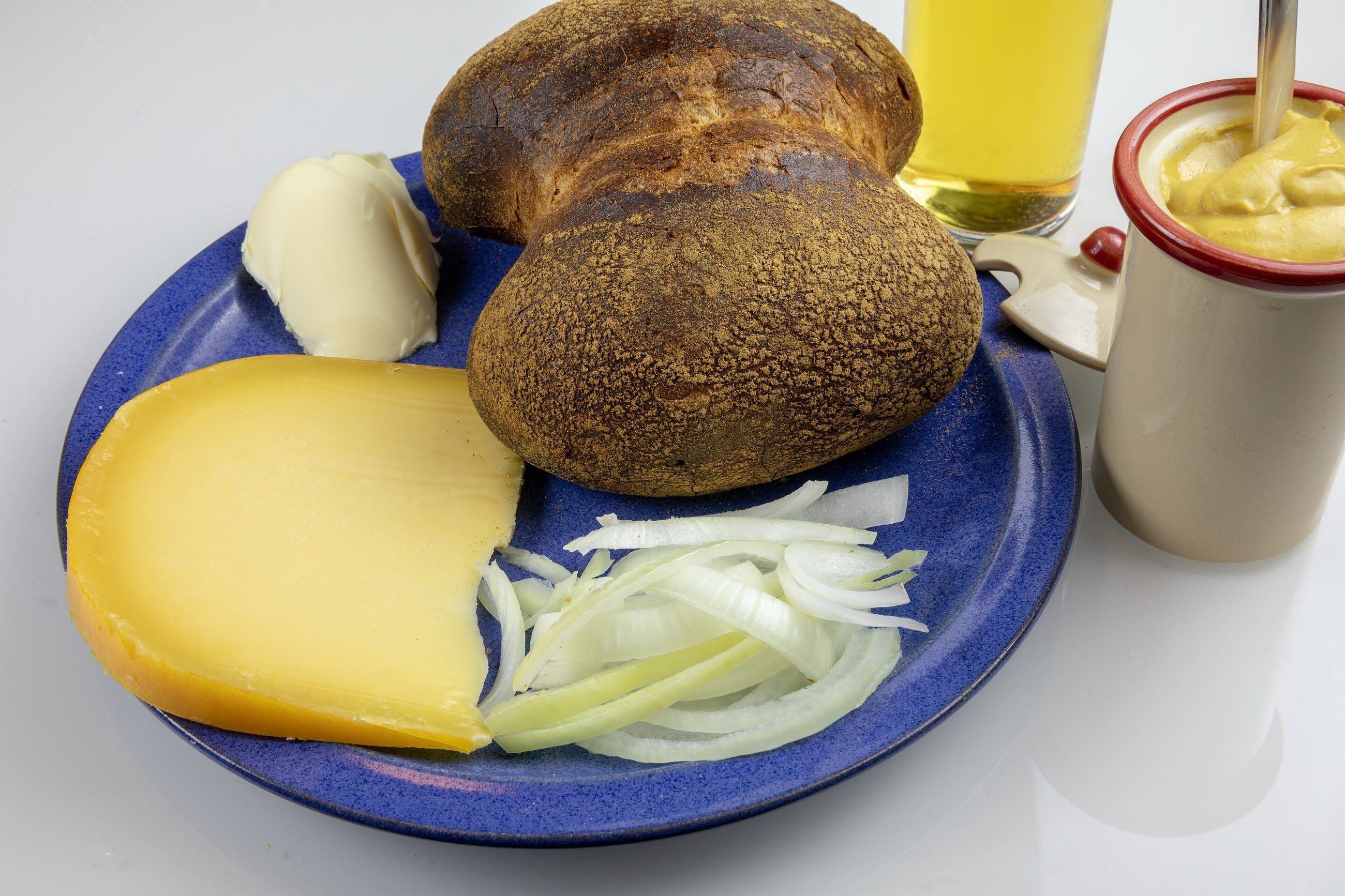 Ein Halve Hahn mit Röggelchen, Gouda, Zwiebelringen und Senf auf einem blauen Teller.