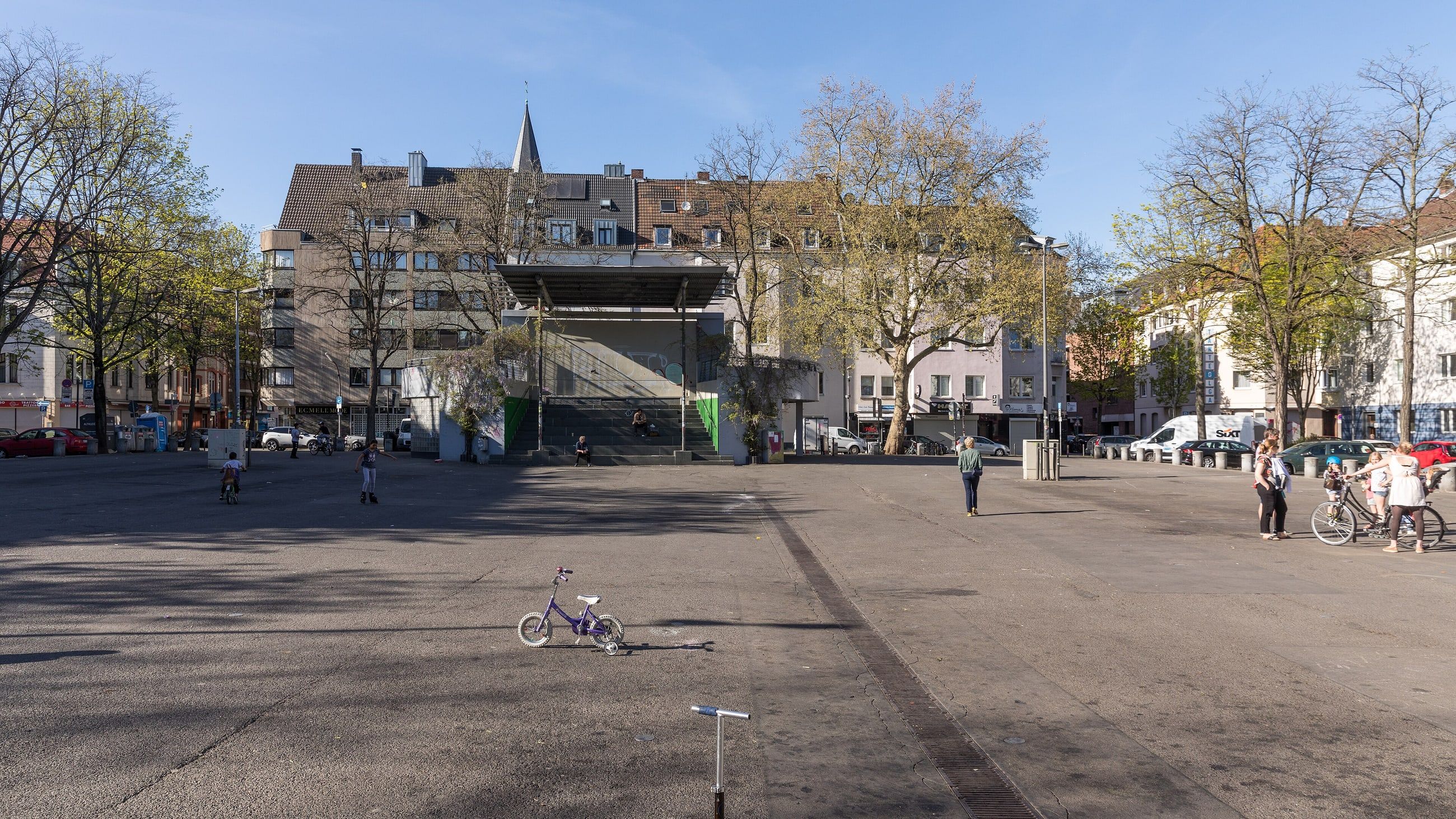 Der weite Wilhelmplatz in Köln-Nippes mit Wohnhäusern und Bäumen im Hintergrund.