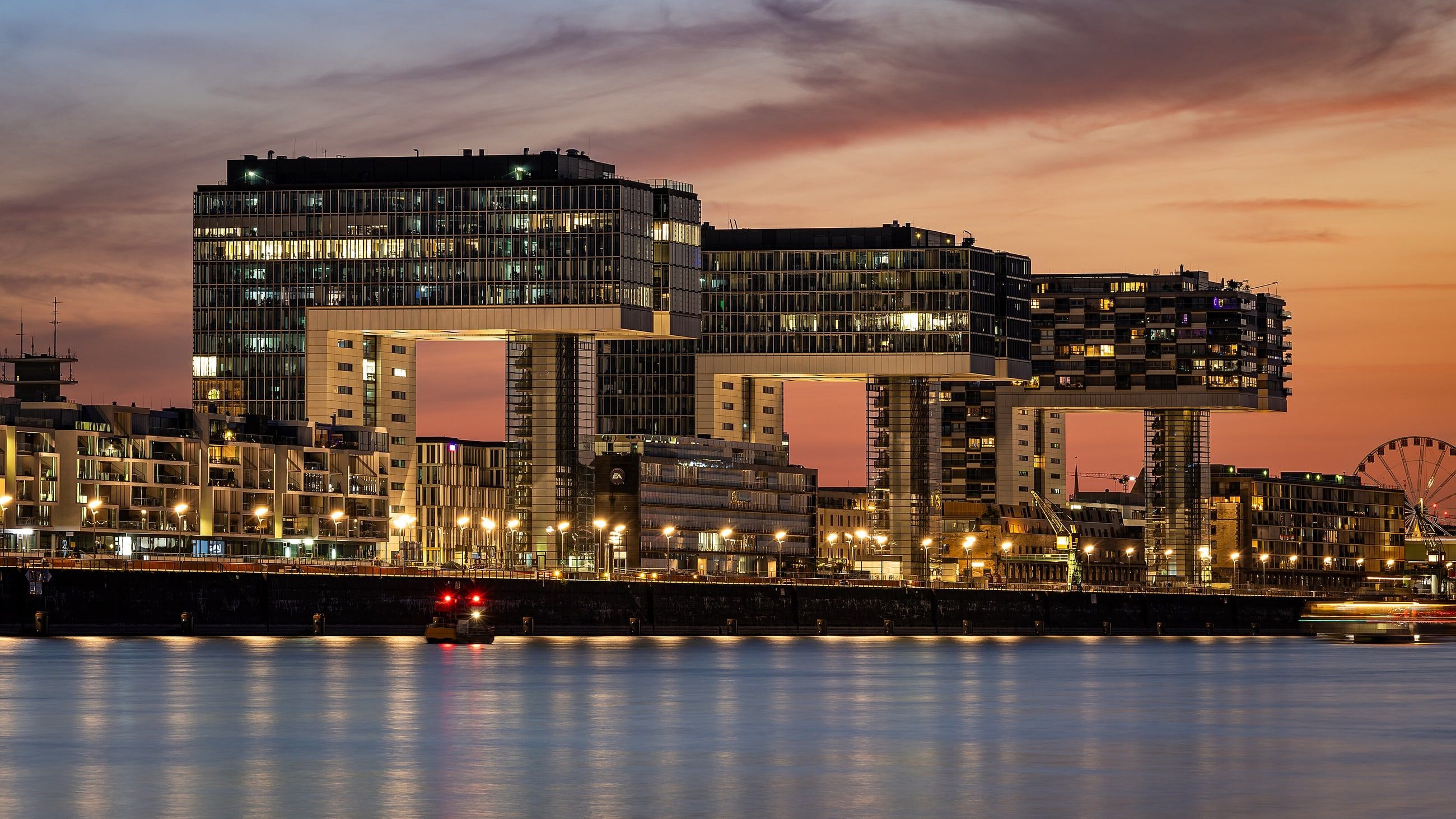 Die Kranhäuser im Kölner Rheinauhafen spiegeln sich in der Abenddämmerung im Rhein.
